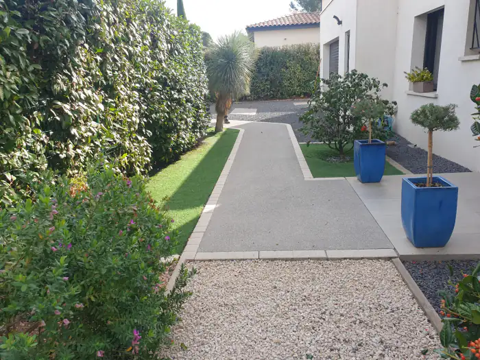 Allée en béton désactivé bordée de pavés, gazon et graviers décoratifs