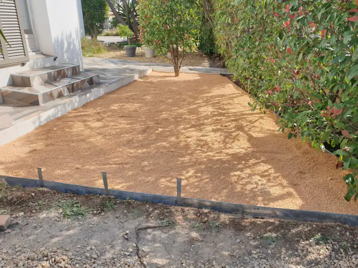 Paillage en gravier beige délimité par une bordure acier au pied d’un escalier