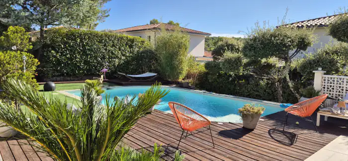Piscine bordée d’une terrasse en bois, palmiers et haie taillée
